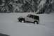 1990 Chevrolet Suburban - Jeep Wrangler navigating a snowy landscape with steep, wooded cliffs in the background.
