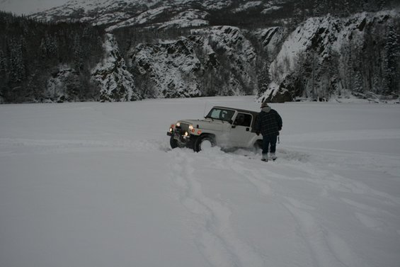 White Jeep Wrangler partially buried in snow, person in plaid jacket standing next to it