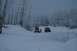 1990 Chevrolet Suburban - Two off-road vehicles are parked in a snow-covered forest clearing with a person standing between them.