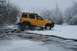 1990 Chevrolet Suburban - A yellow SUV navigates through a partially frozen body of water surrounded by snow-covered trees and bushes.