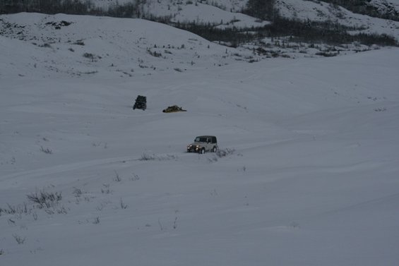 White SUV drives on a snow-covered path with hills in the background