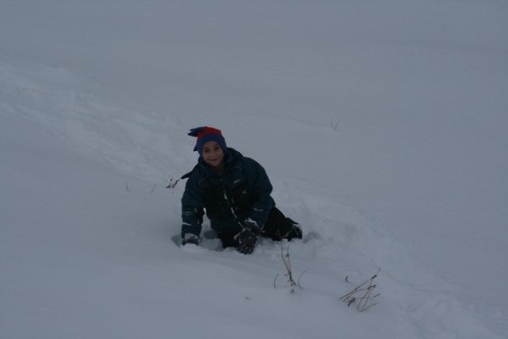 Kid in a blue and red hat and a dark jacket is crawling in deep snow