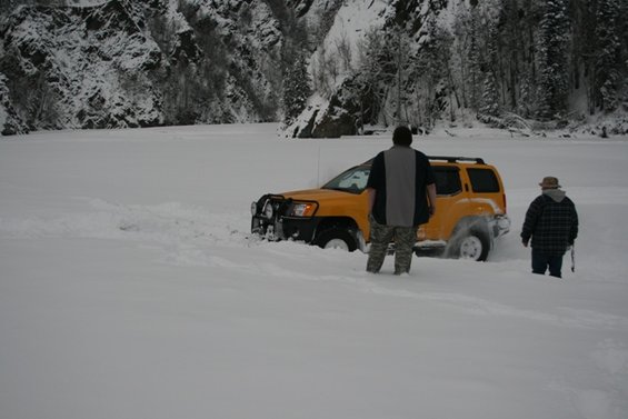 Yellow SUV stuck in deep snow with two people nearby