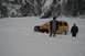 1990 Chevrolet Suburban - A yellow SUV is stuck in a snowy landscape with two individuals observing the situation.