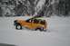 1990 Chevrolet Suburban - A yellow SUV navigates a snow-covered landscape with a mountainous backdrop.