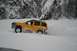 1990 Chevrolet Suburban - A yellow SUV navigates a snowy landscape, kicking up snow as it drives.