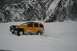 1990 Chevrolet Suburban - A yellow SUV navigates a snowy landscape near a rocky, tree-covered mountainside.