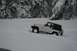 1990 Chevrolet Suburban - A white Jeep Wrangler navigates through a snowy landscape with rocky, snow-covered mountains in the background.