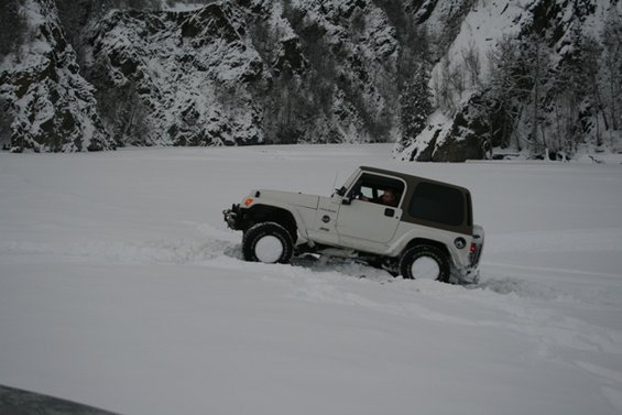 White Jeep Wrangler driving through deep snow with brown top