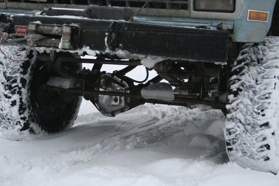 Front axle, suspension, and tires of a vehicle covered in snow. A winch is visible on the front bumper