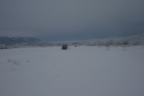 Yellow SUV driving in a snowy landscape under a cloudy sky