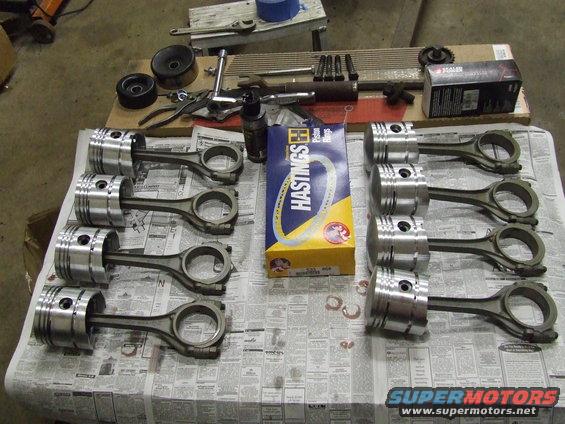 Ten pistons with connecting rods laid out on newspaper, next to a box of Hastings piston rings