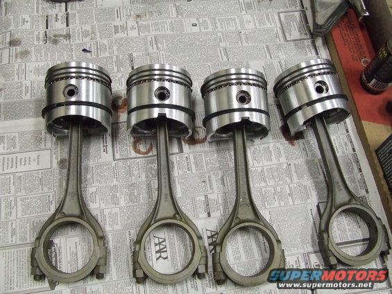four engine pistons with connecting rods laid out on newspaper