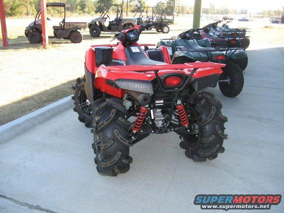 Red Kawasaki ATV with large tires, rear view. Other ATVs and golf carts in background