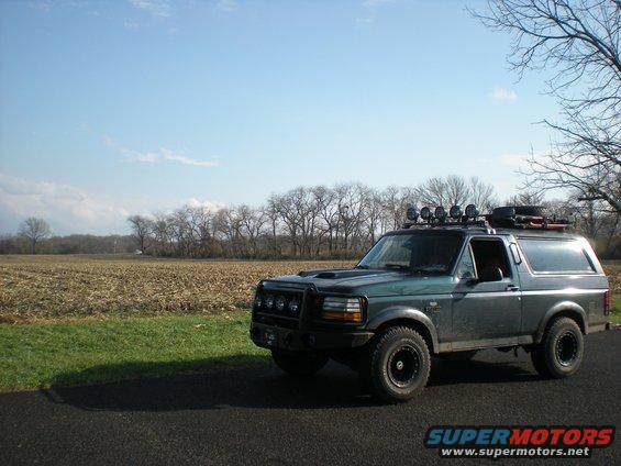 Dark green 1993 Ford Bronco with roof rack and off-road lights parked on asphalt