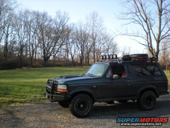Dark green Ford Bronco with roof rack and off-road lights parked on a gravel road
