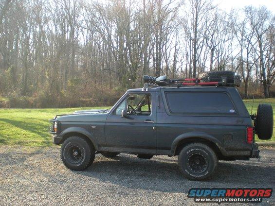 Dark gray SUV, possibly a Ford Bronco, with a roof rack carrying tools and a spare tire. It has aftermarket wheels and a spare tire mounted on the rear