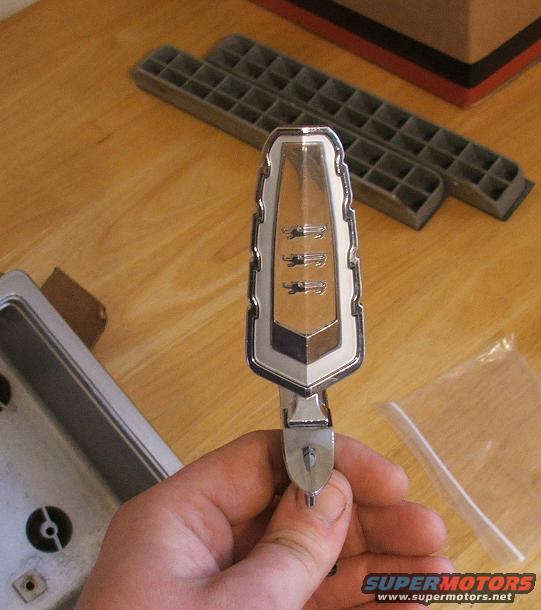 Chrome and gold car emblem with three horizontal lines, held in hand