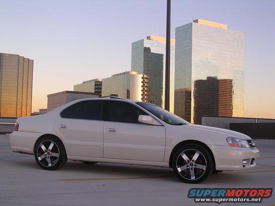 White 2003 Acura TL sedan parked in a lot with skyscrapers in the background at sunset