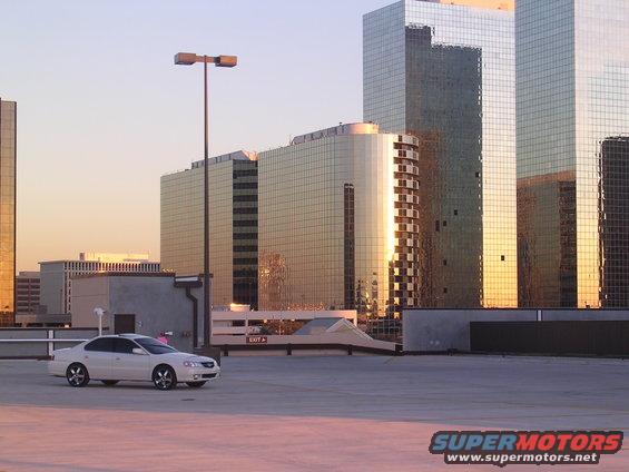 White 2003 Acura TL parked on a rooftop with modern glass buildings in the background