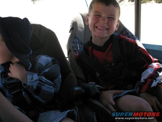 Kid in front seat making a funny face, another kid in car seat next to him