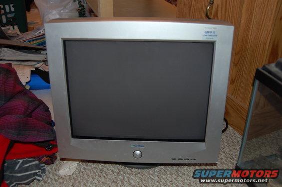Silver CRT television with a dark screen sits on a carpeted floor next to a pile of clothes
