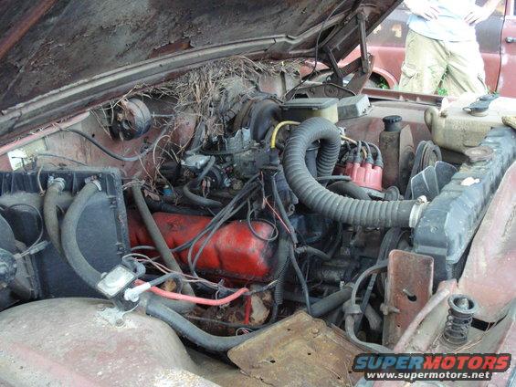 Engine bay of an old Jeep with lots of rust and bird nests. Another vehicle is visible in the background