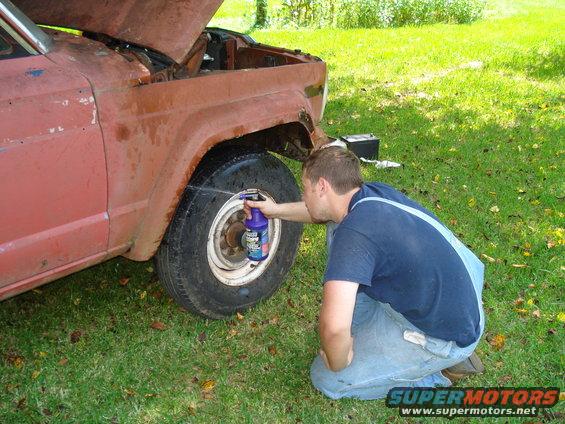Rusty red 1984 Jeep J-10 side view, man spraying tire