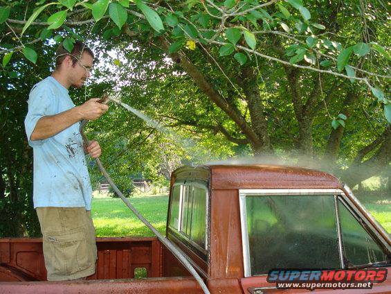 Brown 1984 Jeep J-10 truck cab with chrome trim being washed by a man with a hose