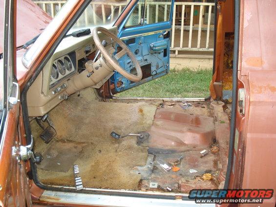 Interior of a Jeep showing the dashboard, steering wheel, and floor. The floor is bare metal with some debris