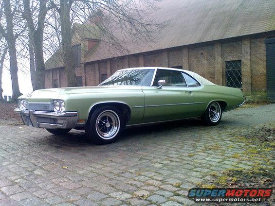 Green 1973 Buick LeSabre coupe parked on cobblestone in front of a brick building
