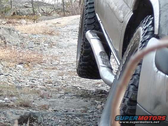 Close-up of a truck's side step and aggressive tire tread on a gravelly surface