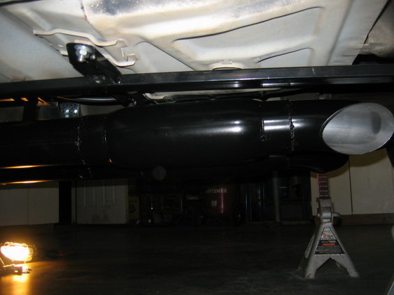 Underside view of a car's exhaust system, including a muffler and tailpipe, supported by jack stands