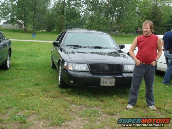 Black Mercury Grand Marquis with a man standing next to it. Another car is partially visible on the left
