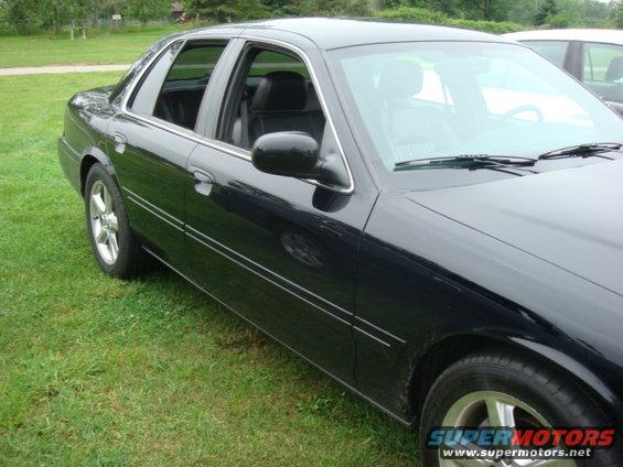 Black sedan parked on grass, front 3/4 view. Chrome trim along the side and on the wheels