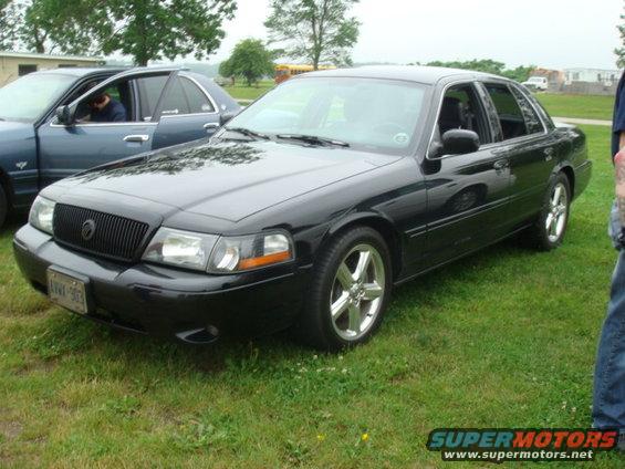 Black 2004 Ford Crown Victoria sedan, 3/4 front view. Another blue sedan is parked to the left