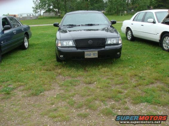 Black sedan with a dark grille and license plate AVWX-903 parked on grass