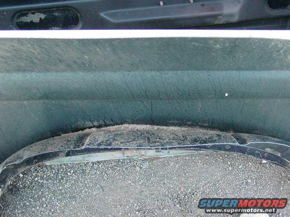 Dark green vehicle wheel well with gravel and a damaged black fender flare