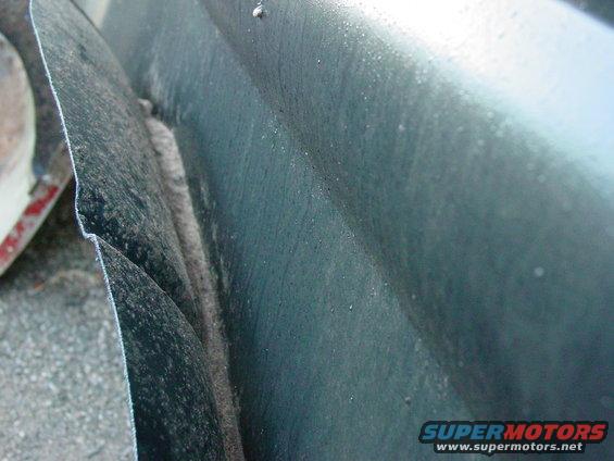 Close-up of a dark green fender edge and wheel well area, showing dirt and wear