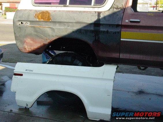 White fender panel attached to a maroon and black Ford Bronco with yellow stripe, showing rust and damage