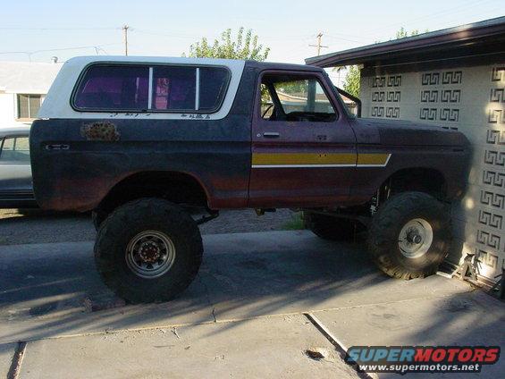 Lifted Ford Bronco with a two-tone paint job and large off-road tires parked next to a building