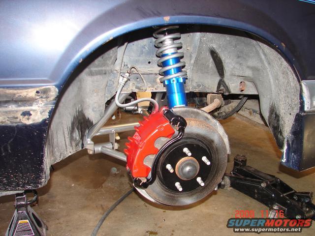 1985 Ford Mustang front wheel assembly with red brake caliper and blue coilover suspension