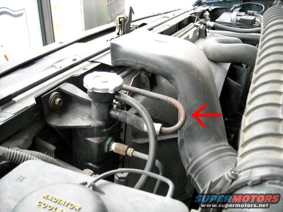 1994 Ford Bronco engine bay showing radiator, hoses, and air intake tube. Red arrow points to a metal hose