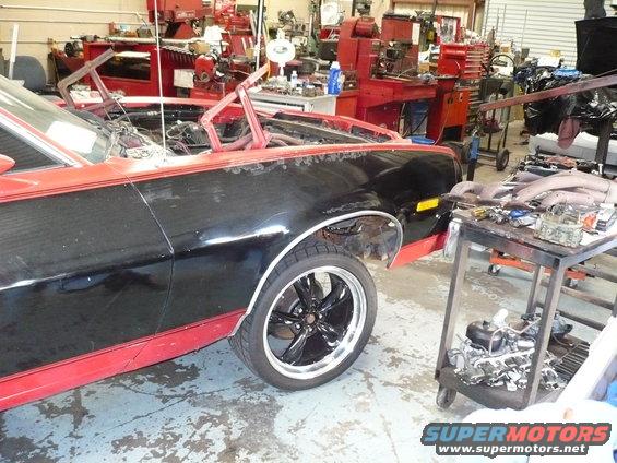 Black and red pickup truck with custom wheels, hood open, in a workshop