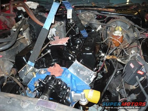 Engine bay with engine partially installed, straps holding it up. Edelbrock valve covers visible