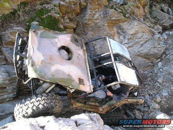 Off-road buggy tipped on its side in rocks with a person inside