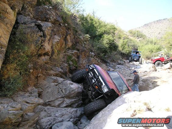 Red 1986 Toyota Hilux stuck on rocks with two other off-road vehicles visible