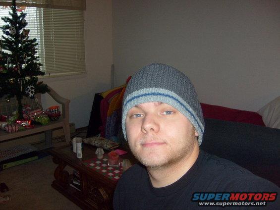 guy wearing a gray beanie with blue stripes, indoors near a Christmas tree and coffee table