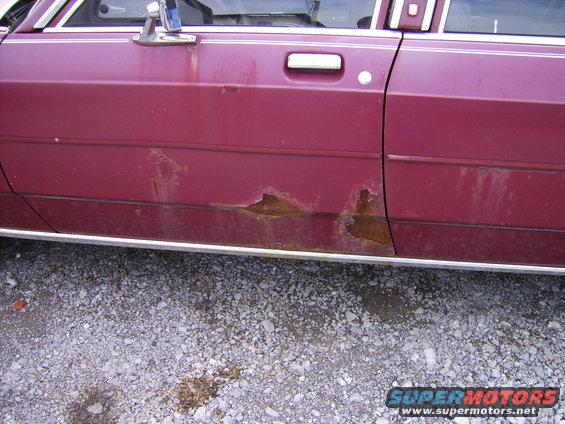 maroon sedan door showing significant rust damage along the lower body panel and trim
