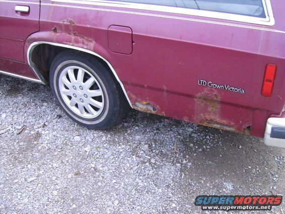 Maroon 1988 Ford LTD Crown Victoria wagon rear quarter panel with significant rust and a partial view of the wheel